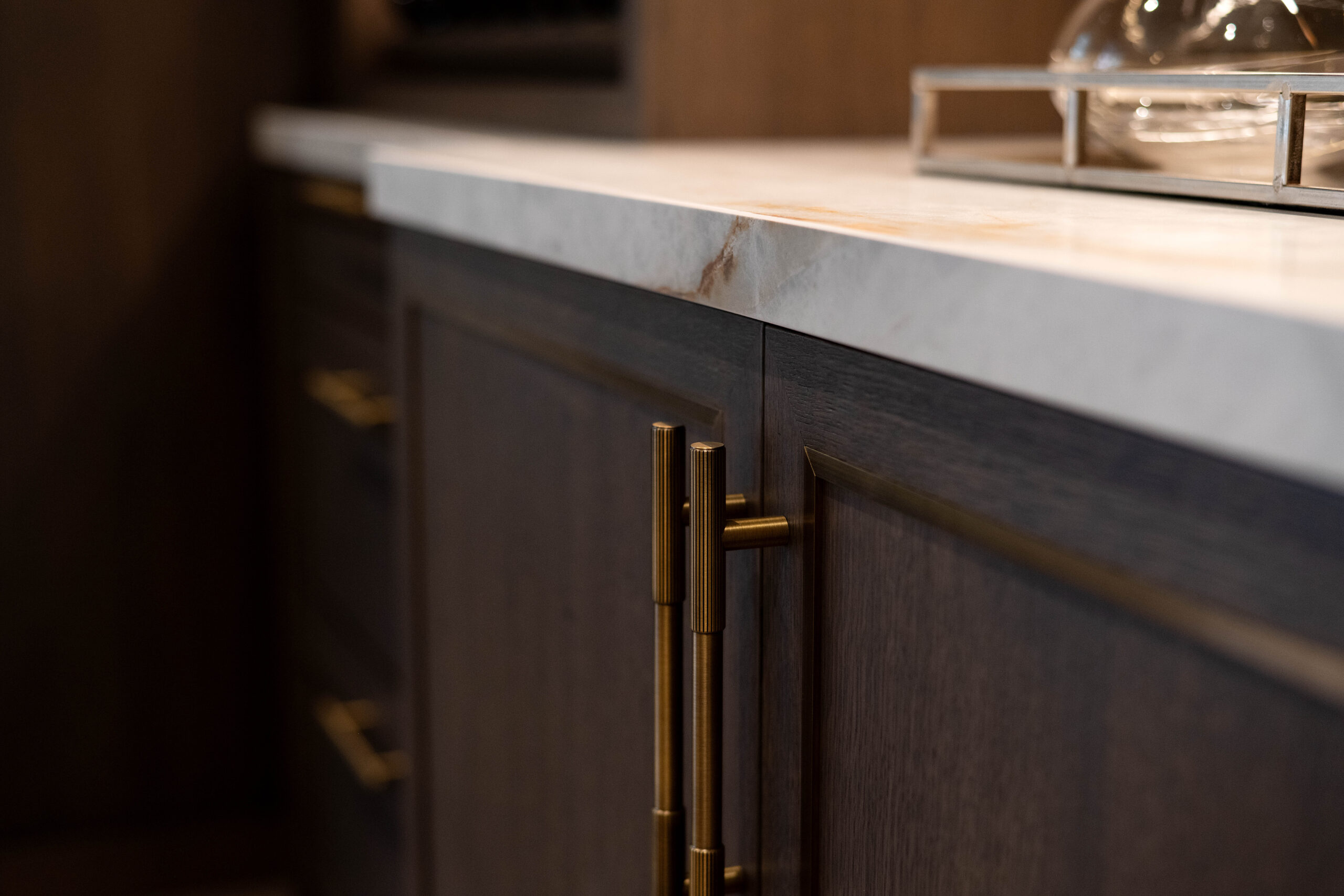 in the dinning room, Dark wood cabinets with sleek, vertical brass handles are topped by a white marble countertop. A delicate, elegant ambiance is suggested.