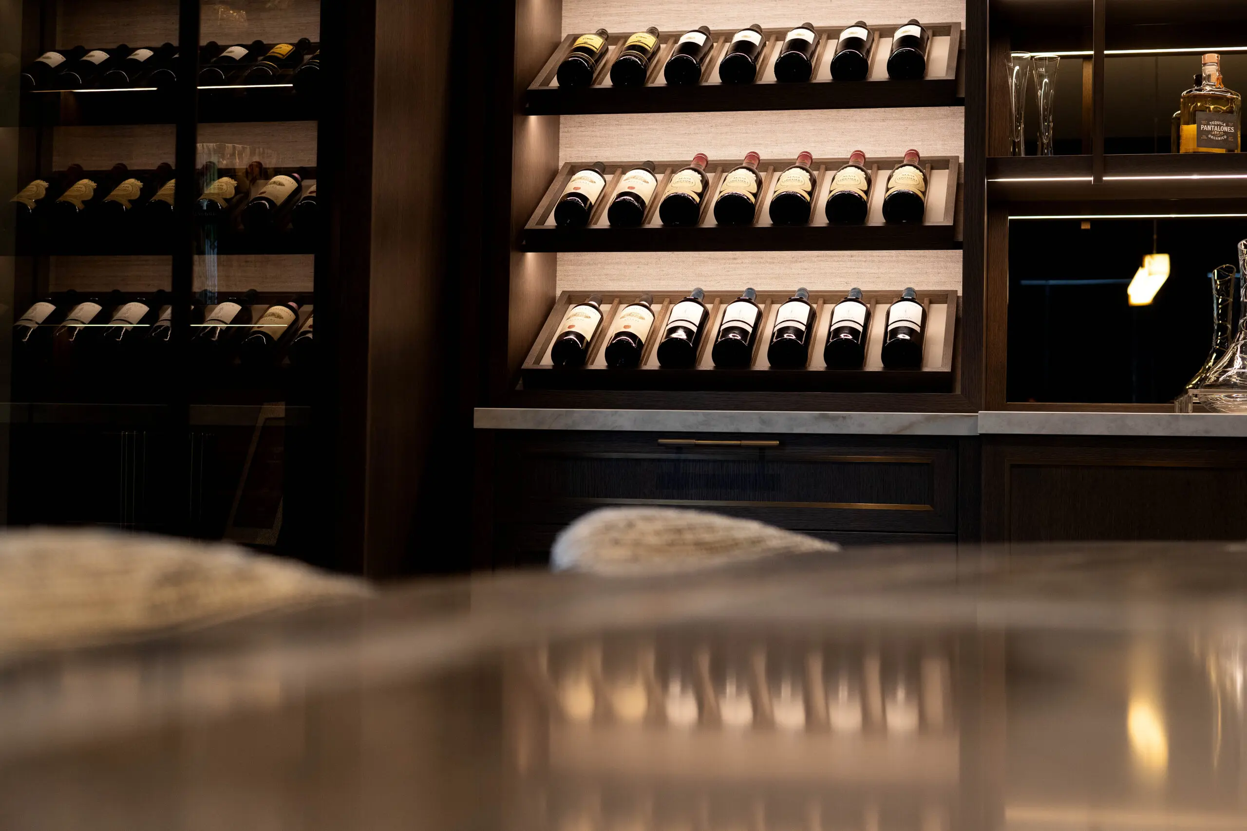 Elegant wine rack in the dinning room, the interior features neatly arranged wine bottles on wooden shelves, a soft warm ambiance, and sleek marble countertop reflections.