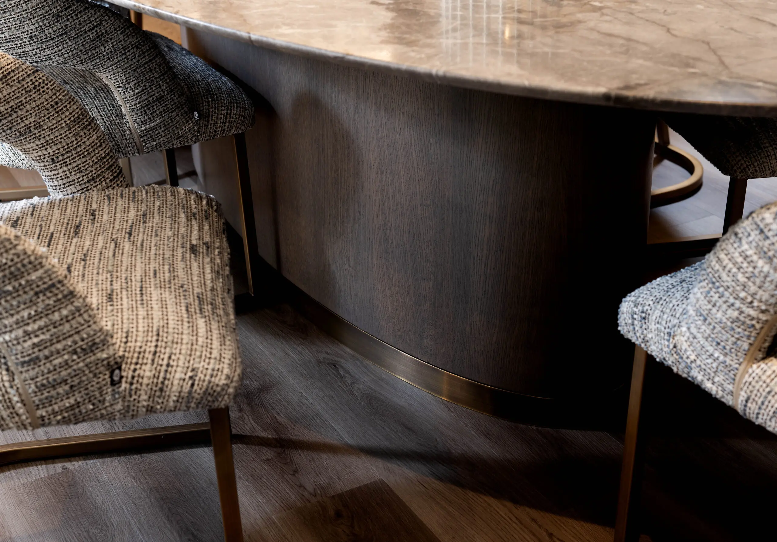 A close-up of a modern dining setup features textured gray fabric chairs around a dark, curved wooden table with a polished marble top on a wood floor.