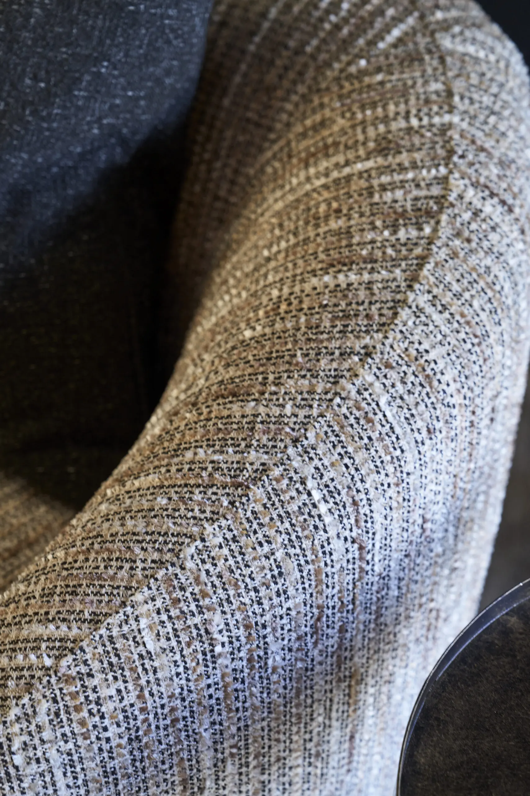 Close-up of a textured, striped brown and beige fabric armchair with a black cushion. The setting conveys a cozy, inviting atmosphere.