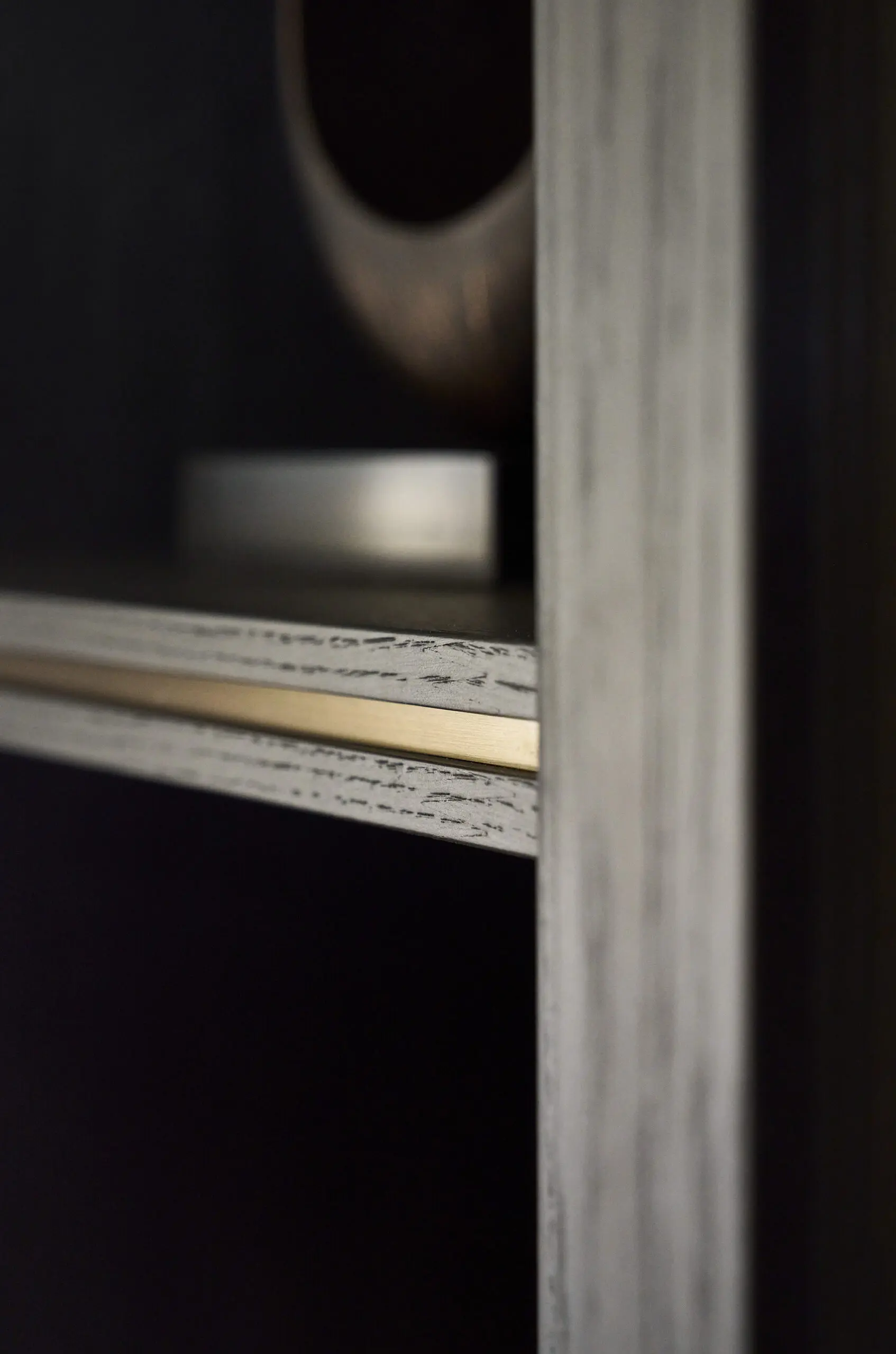 Close-up of a black and wood-textured shelf edge with a metallic strip, casting a subtle shadow. The background is softly blurred, suggesting minimalism.