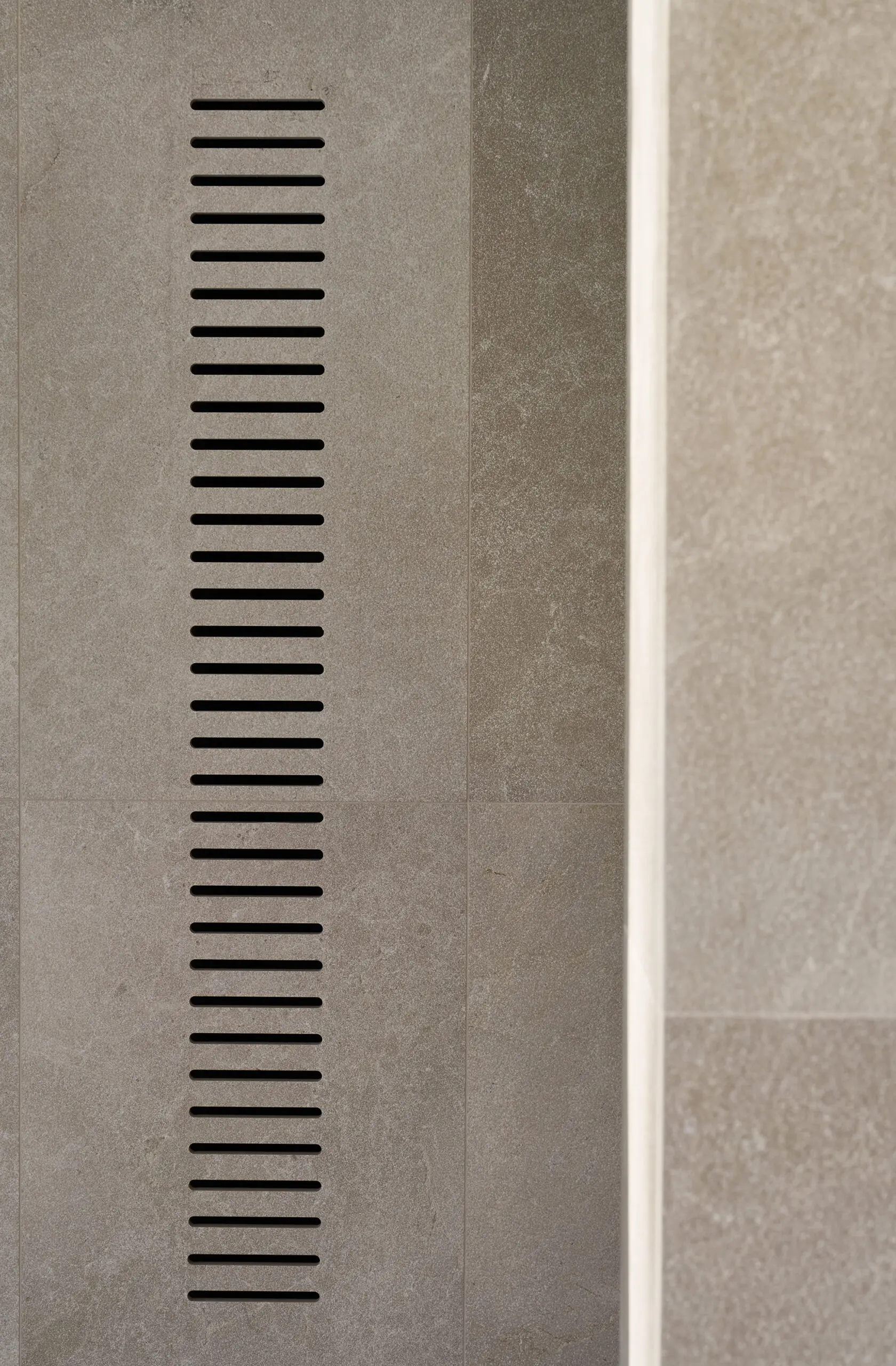 Vertical vent with horizontal slits set on a smooth, beige stone wall. Minimalist design conveys simplicity and modernity.