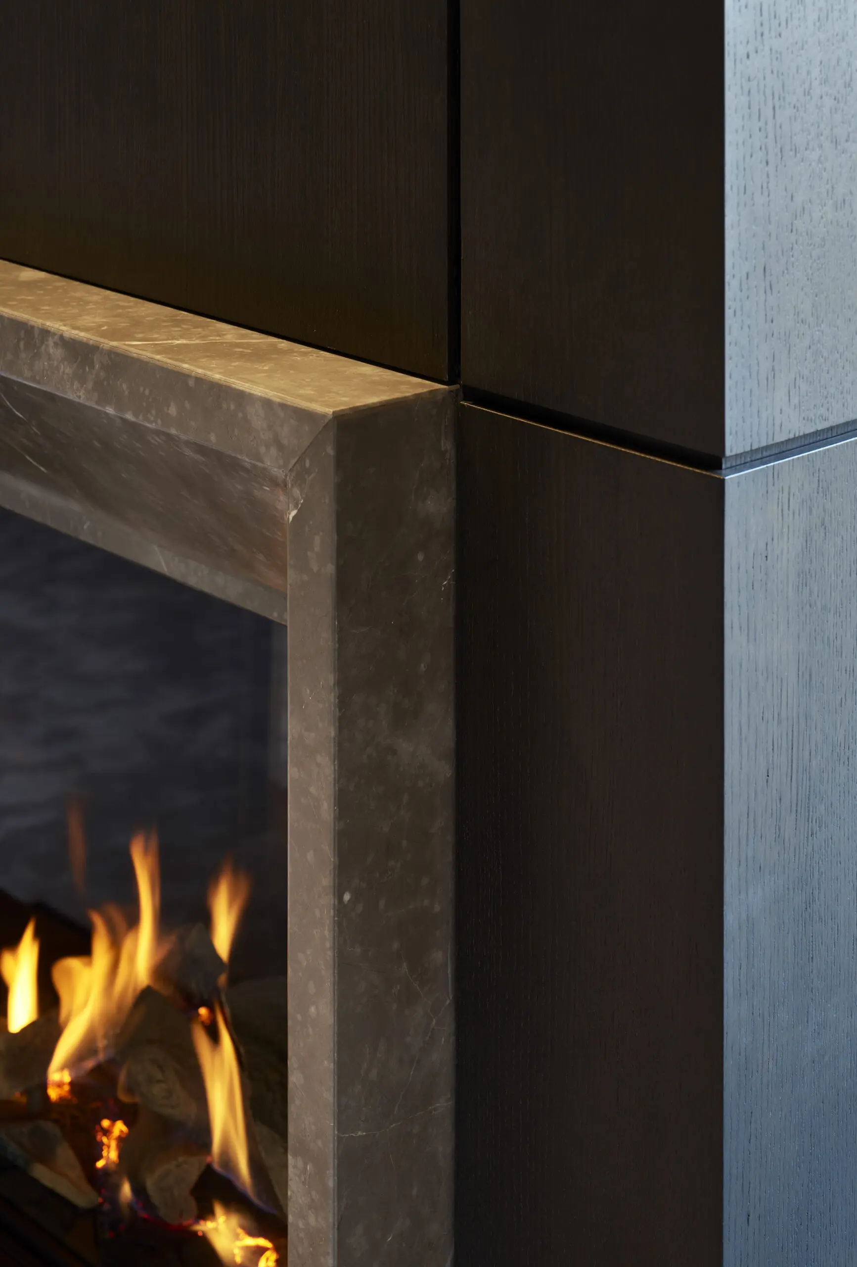 Close-up of a modern fireplace with dark wooden panels and sleek marble trim. Bright flames flicker over logs, creating a warm and inviting atmosphere.
