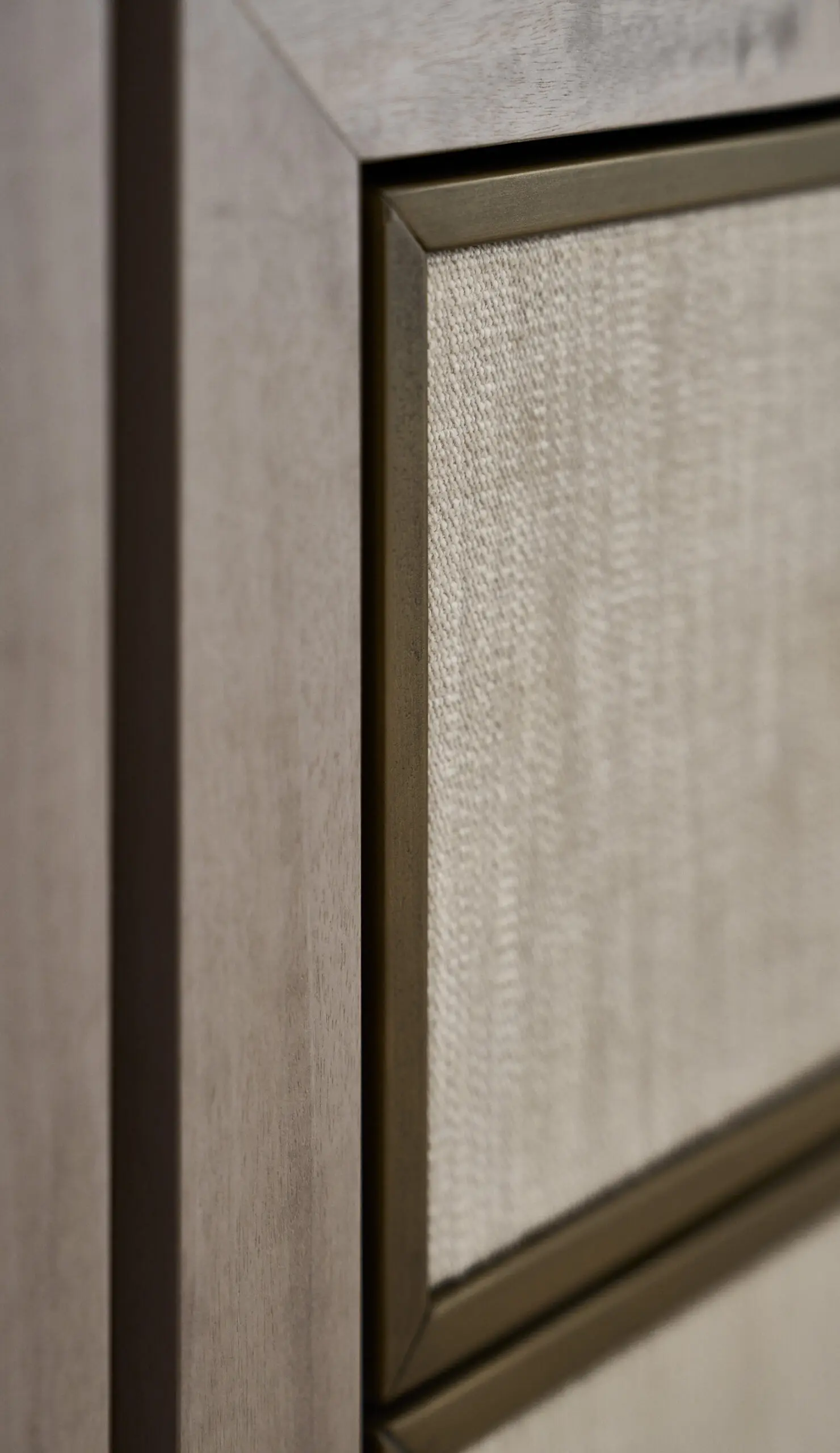 Close-up detail of a modern interior wall panel featuring textured beige fabric inset panels framed with slim metallic trim and warm wood finishes, showcasing refined contemporary craftsmanship.