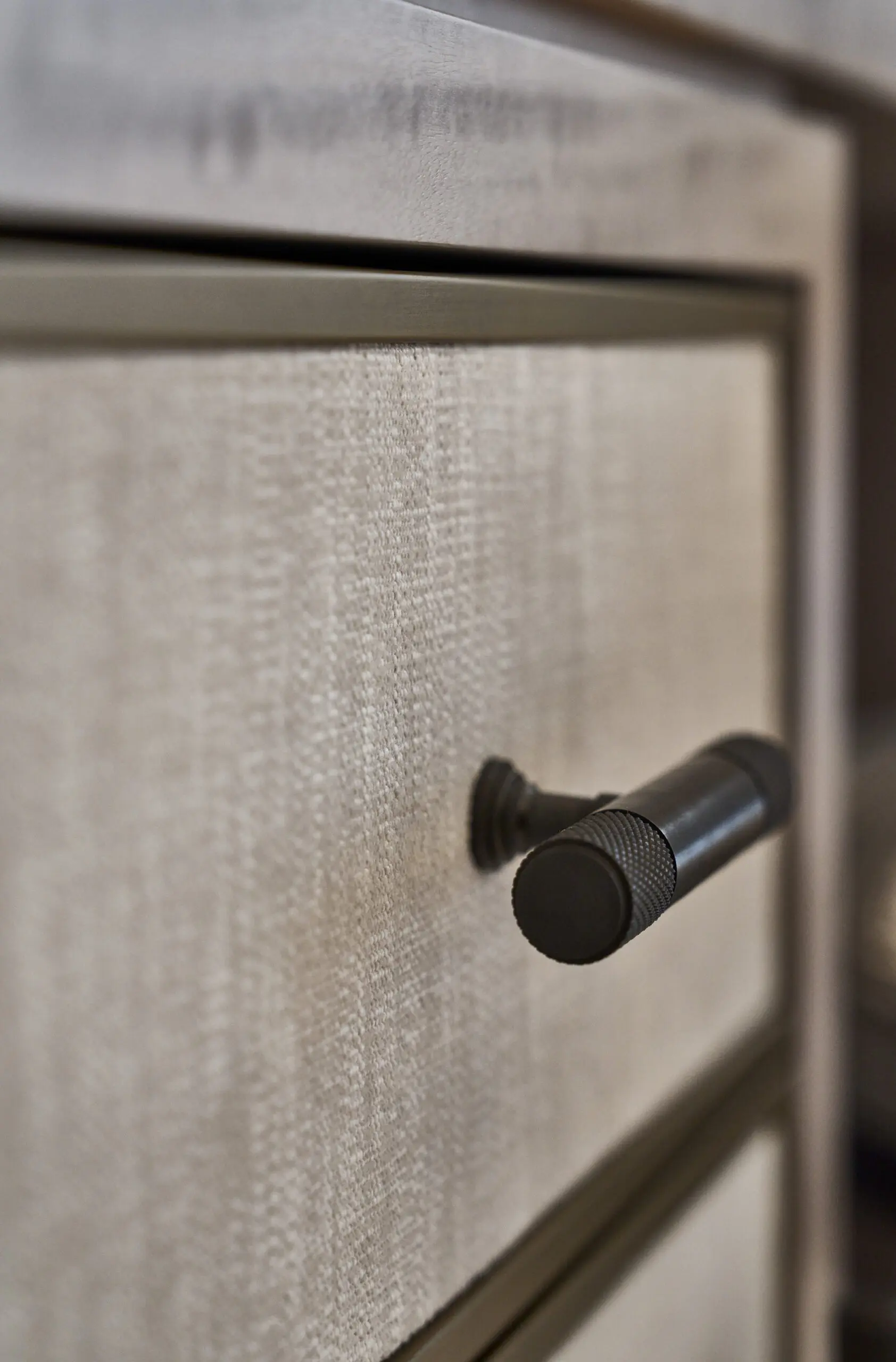 Close-up of a cabinet with a textured beige surface and a cylindrical metal handle. The sleek design gives a modern, minimalist feel.